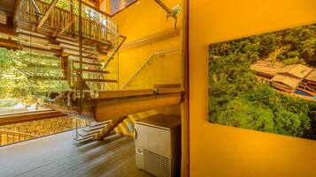 Una escalera de madera con balaustrada de vidrio que conduce a un balcón, un equipo de aire acondicionado pequeño y un cuadro con la imagen de un vehículo en la pared.