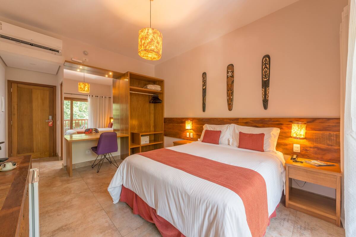 A well-lit bedroom with a large bed, a desk, and a chair. There are wall-mounted lights and a ceiling light.