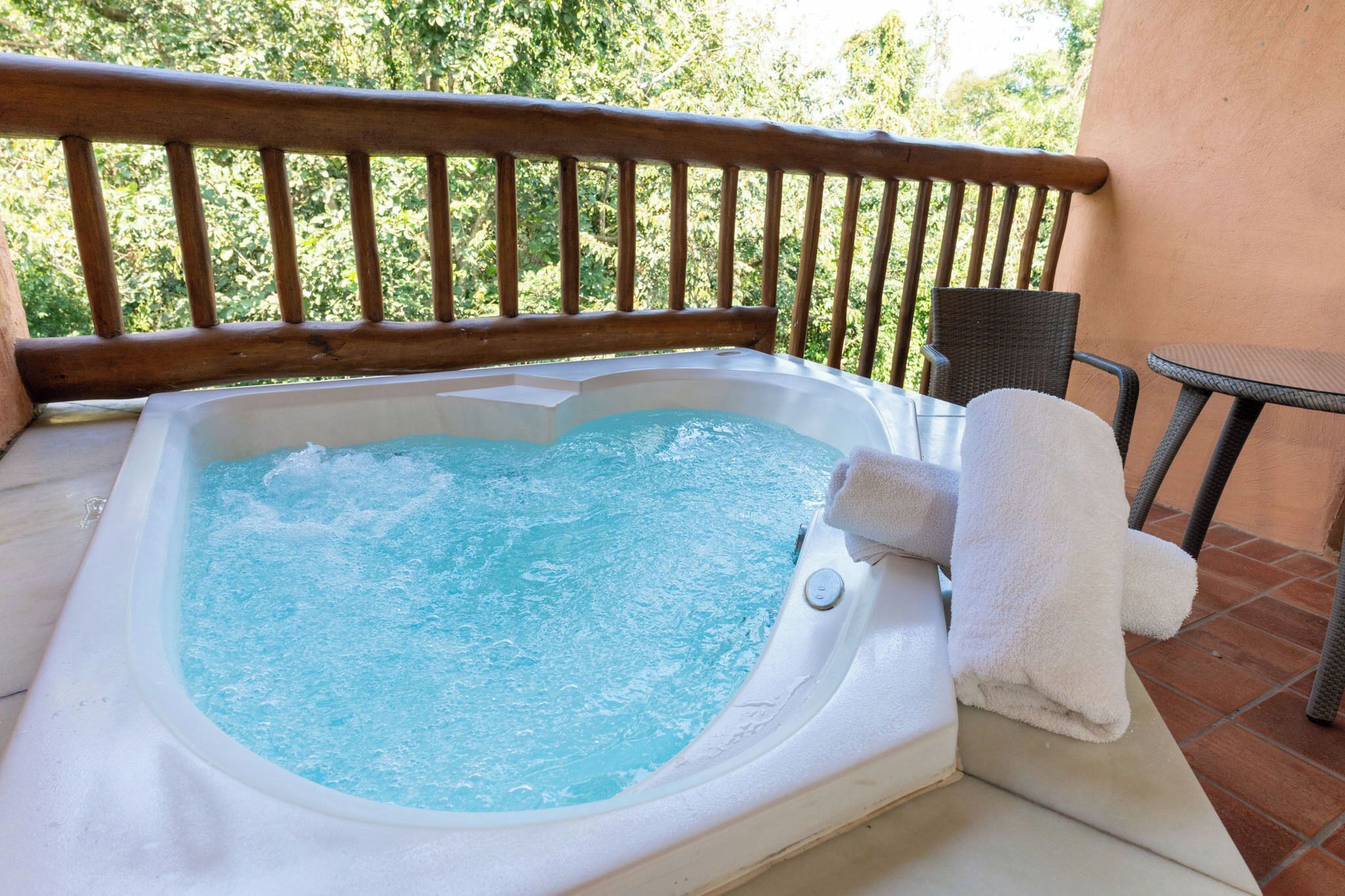 Un jacuzzi en un balcón con barandilla de madera, una silla y una mesita.
