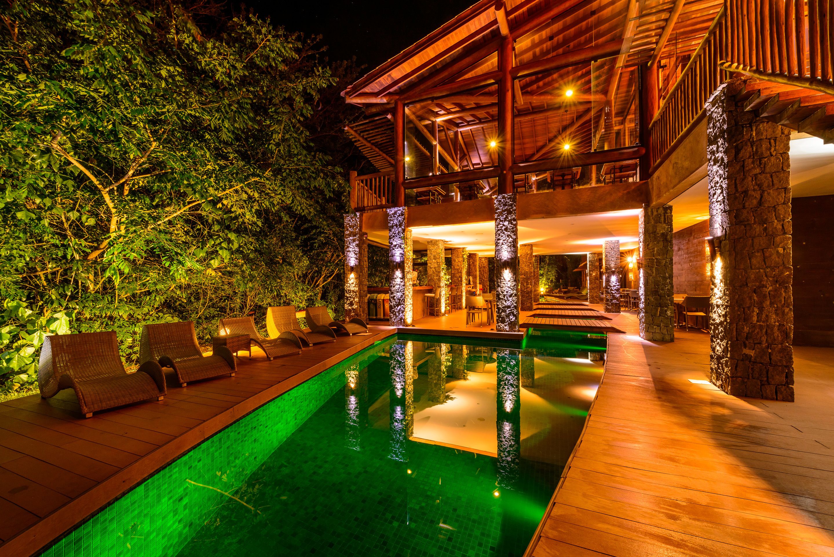 Un espace aménagé au bord de la piscine, avec des chaises longues, une terrasse en bois et un bâtiment doté d’un patio couvert.