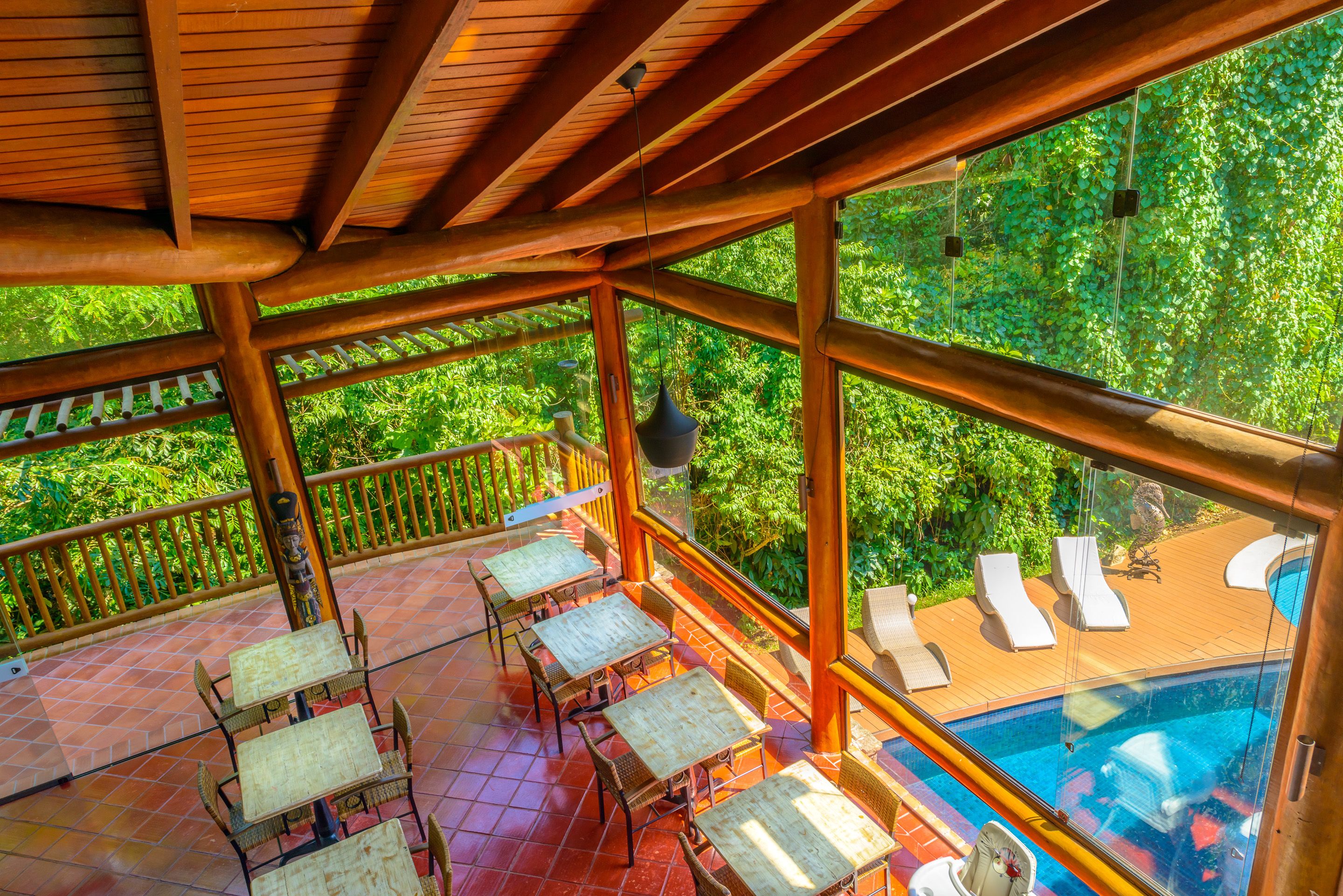A covered outdoor area with wooden furniture and a pool.