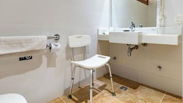 Casa de banho com sanita, lavatório, espelho e uma cadeira branca com rodas.