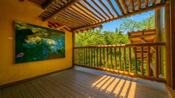 Une terrasse en bois avec une balustrade en bois, une grande peinture représentant un paysage aquatique et une vue sur les arbres à travers la balustrade.