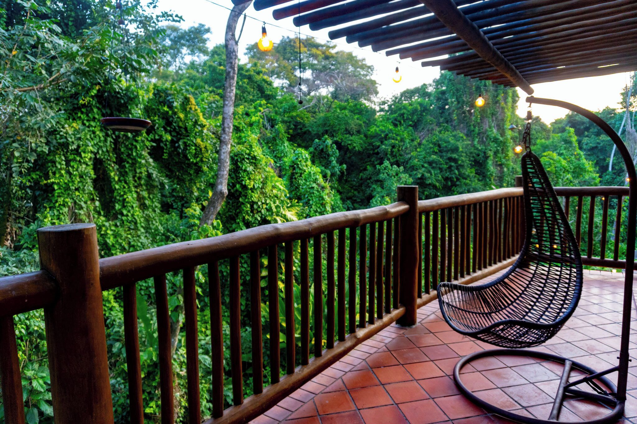 A wooden balcony with a metal chair and a hanging light fixture.