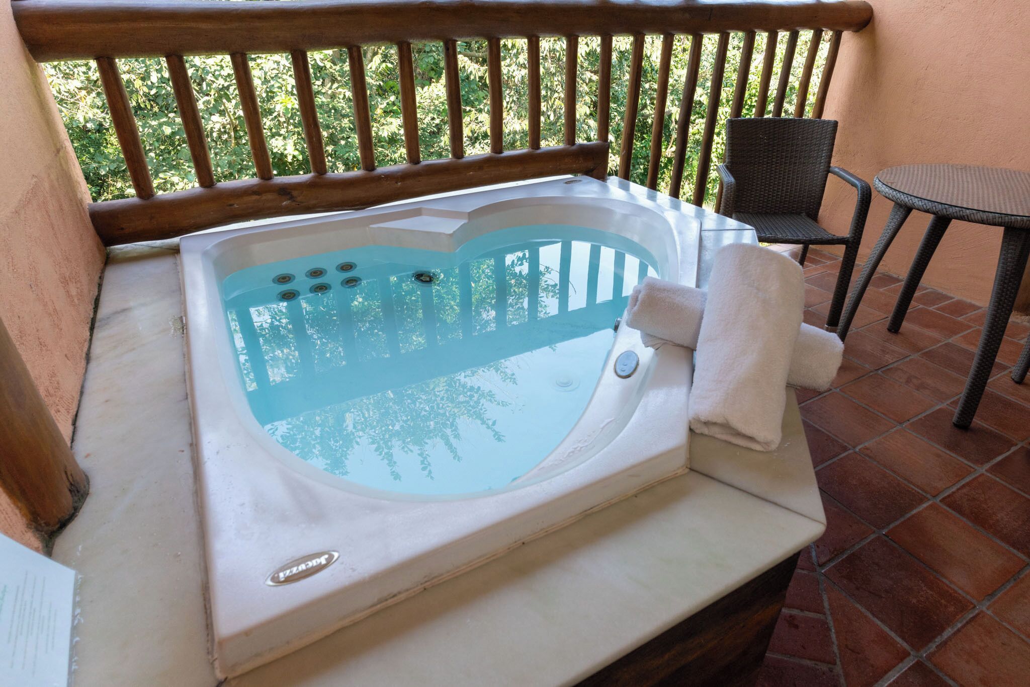 Un jacuzzi sur un balcon doté d’une rambarde en bois, d’une chaise et d’une petite table.