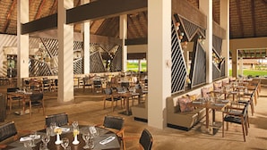 Un restaurant spacieux avec de hauts plafonds et un toit de chaume. Les tables sont dressées avec des verres à vin et des couverts.