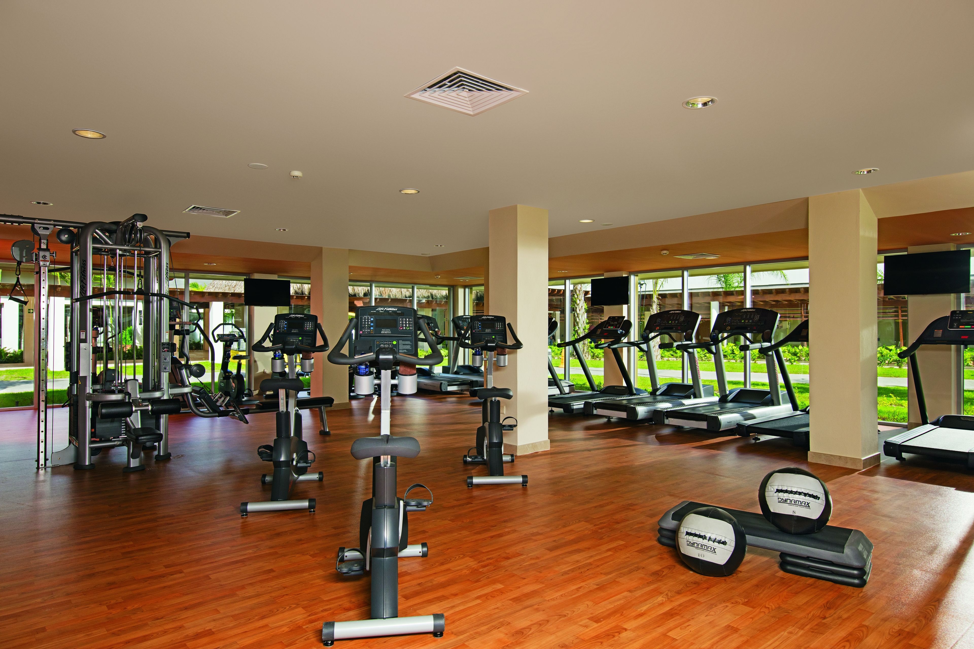 Une salle de sport spacieuse, dotée de divers équipements d’exercice, notamment des tapis de course et des appareils de musculation, et de grandes fenêtres offrant une vue sur l’extérieur.
