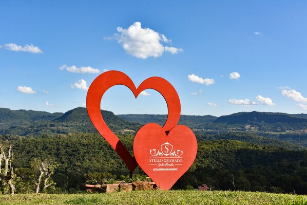 Um sinal em forma de coração vermelho com um logotipo e texto, com uma paisagem montanhosa ao fundo.