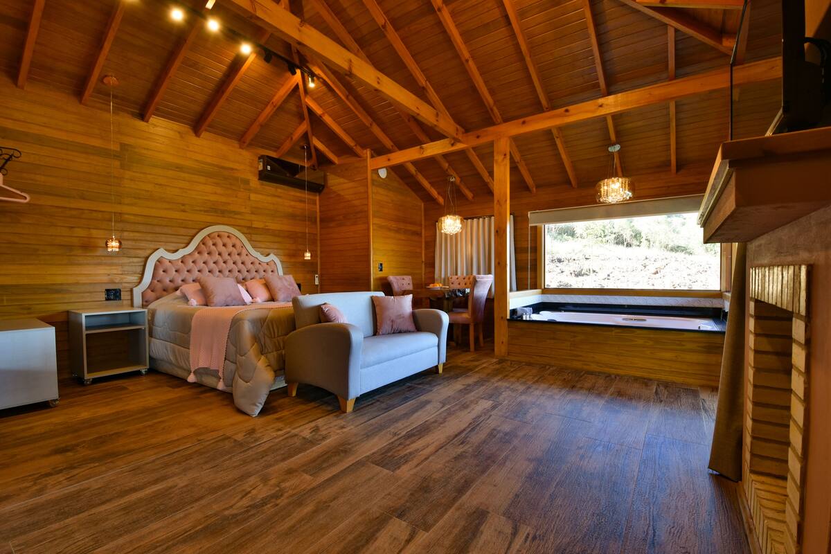 A cozy bedroom with a large bed, wooden walls, and a window overlooking a natural landscape.
