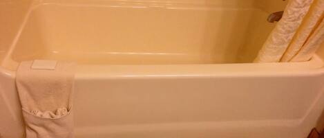 A standard white bathtub with a towel hanging on the side, a shower curtain, and a wooden floor.