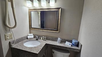 Un baño con lavamanos de encimera de granito, inodoro blanco, espejo con marco dorado y secador de pelo en la pared.