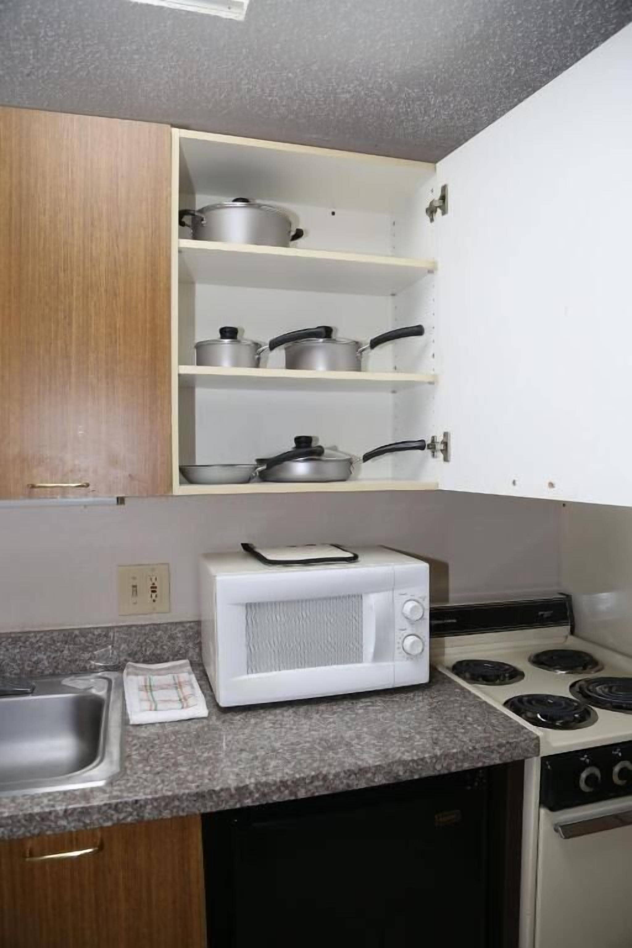 A kitchen with a microwave, stove, and shelves with pots and pans.