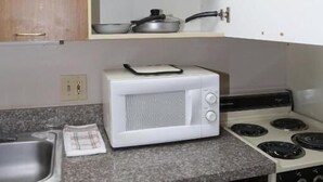 Une cuisine équipée d’un four à micro-ondes, d’une cuisinière et d’étagères où sont rangées des casseroles et des poêles.