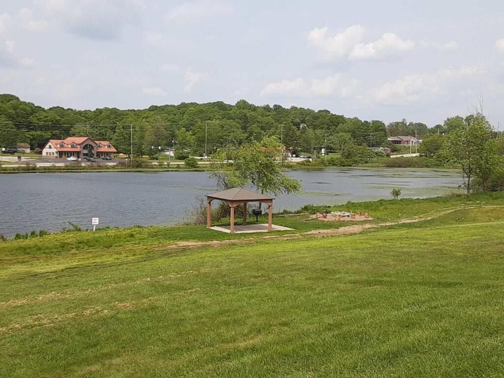A lakeside view with a gazebo, grassy area, and a house in the background.
