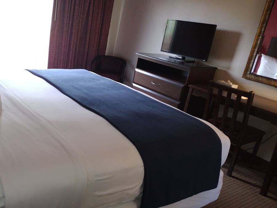 Quarto de hotel com uma cama grande, uma escrivaninha com televisão, uma cadeira e um espelho.