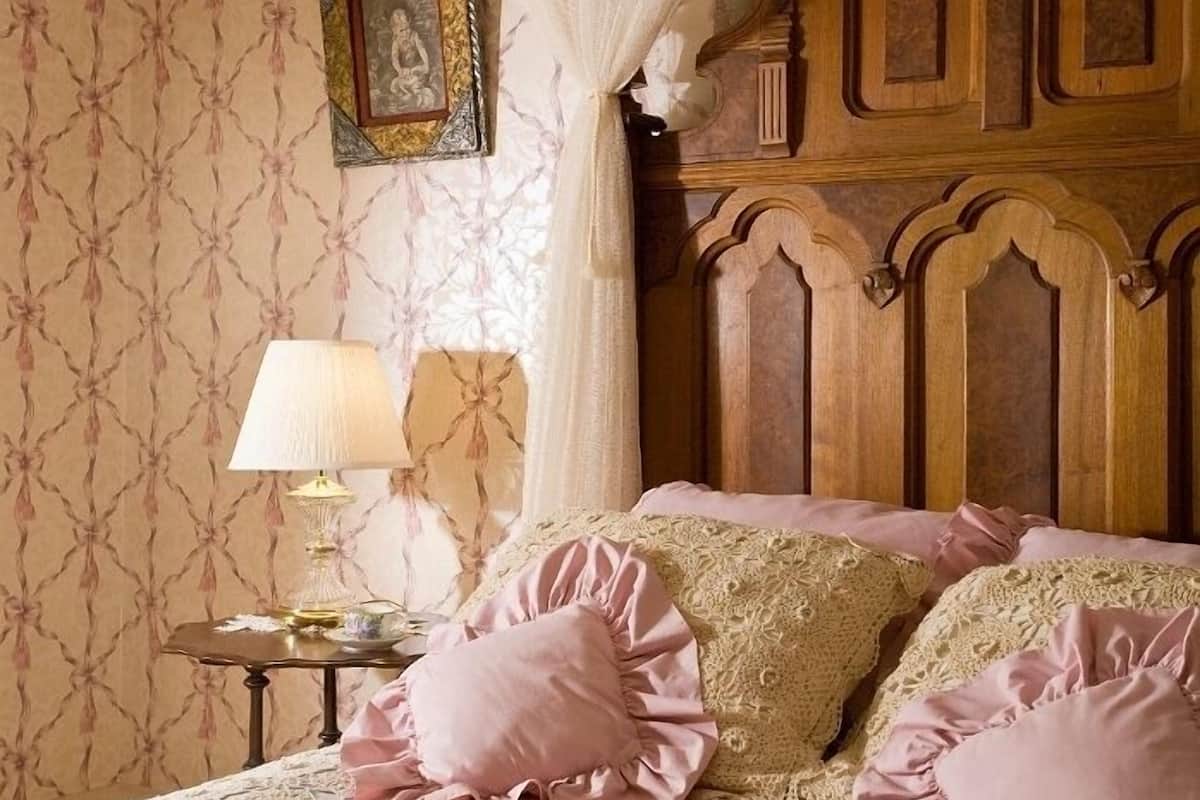 A bedroom with a wooden headboard, a lace bedspread, and pink pillows.