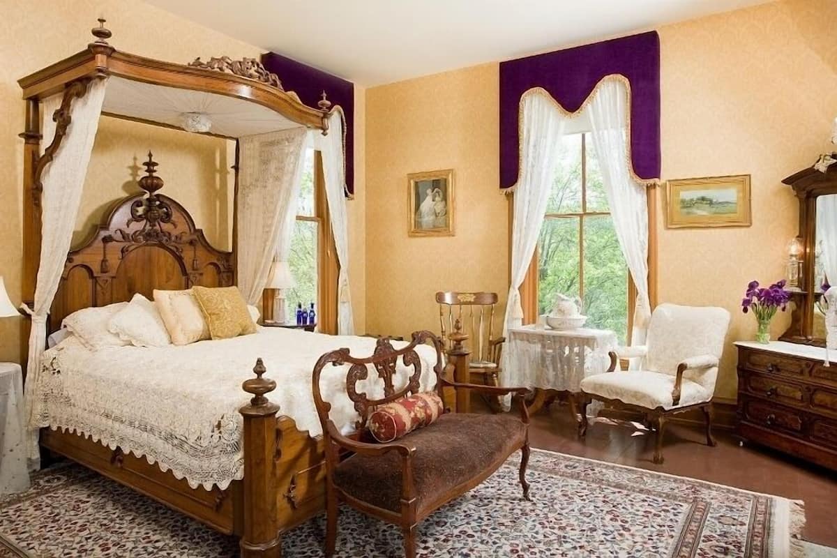 A traditional bedroom with a four-poster bed, a wooden bench, a small table, and a chair.