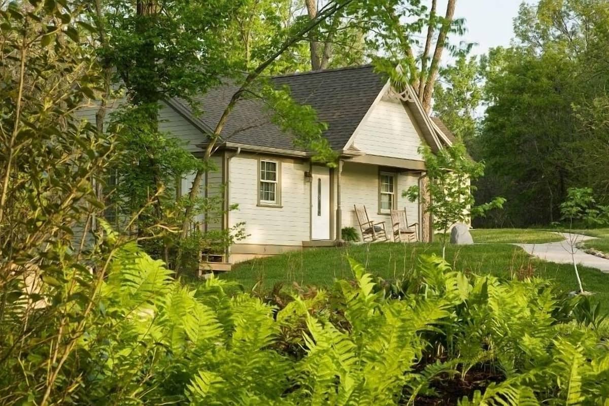 A single-story house with a gabled roof, surrounded by lush greenery and a well-maintained lawn.