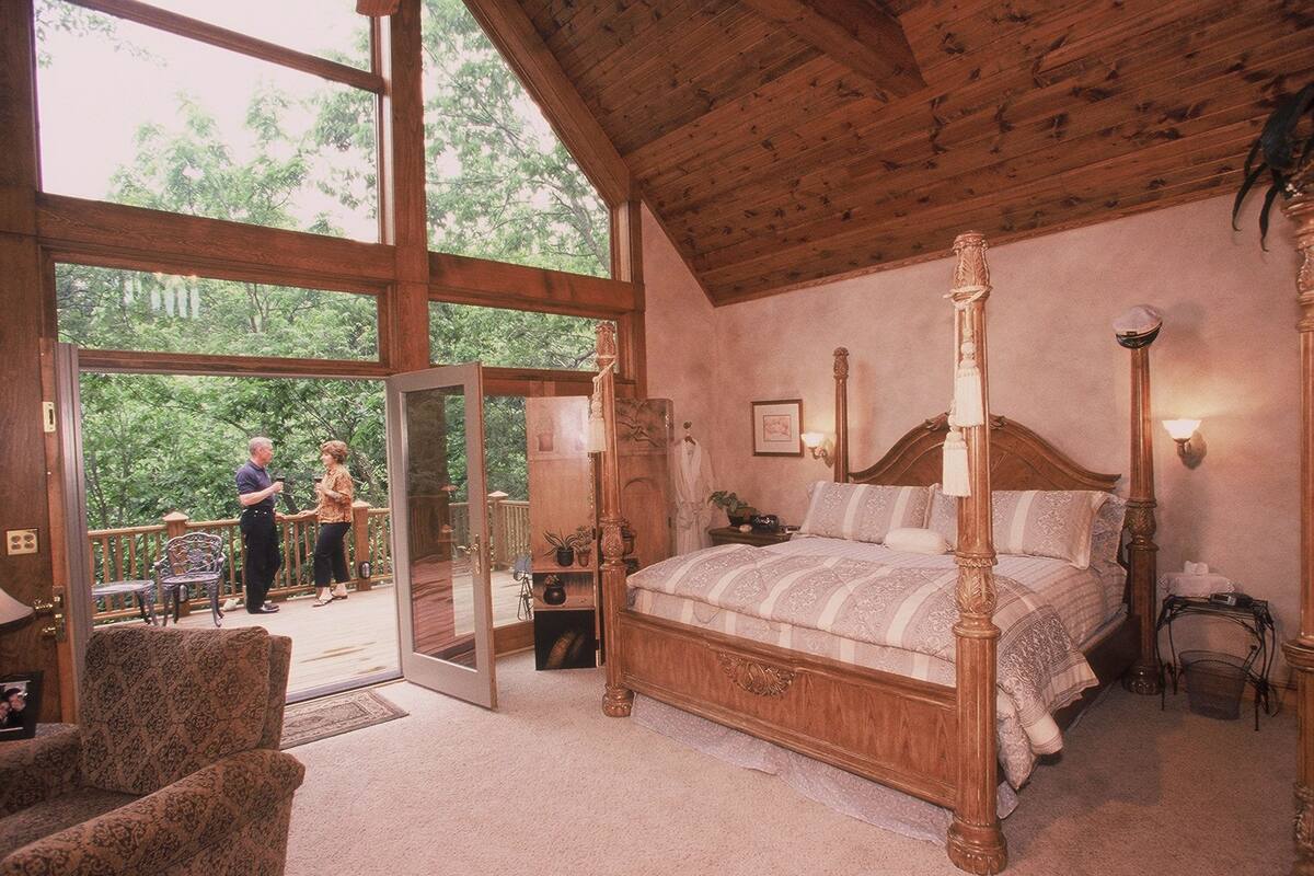 A spacious bedroom with a four-poster bed, a large window, and a balcony.