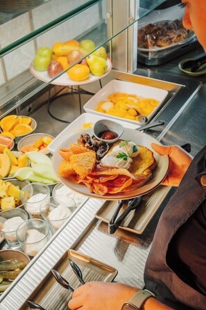 A buffet setup with various food items including fruits, chips, and a plate with a sandwich and a drink.