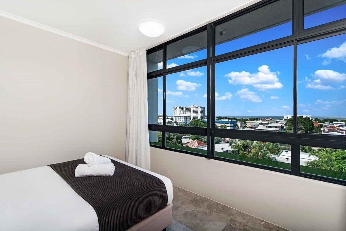 Habitación de hotel con un amplio ventanal que ofrece vistas a la ciudad, una cama bien hecha y un diseño moderno y limpio.