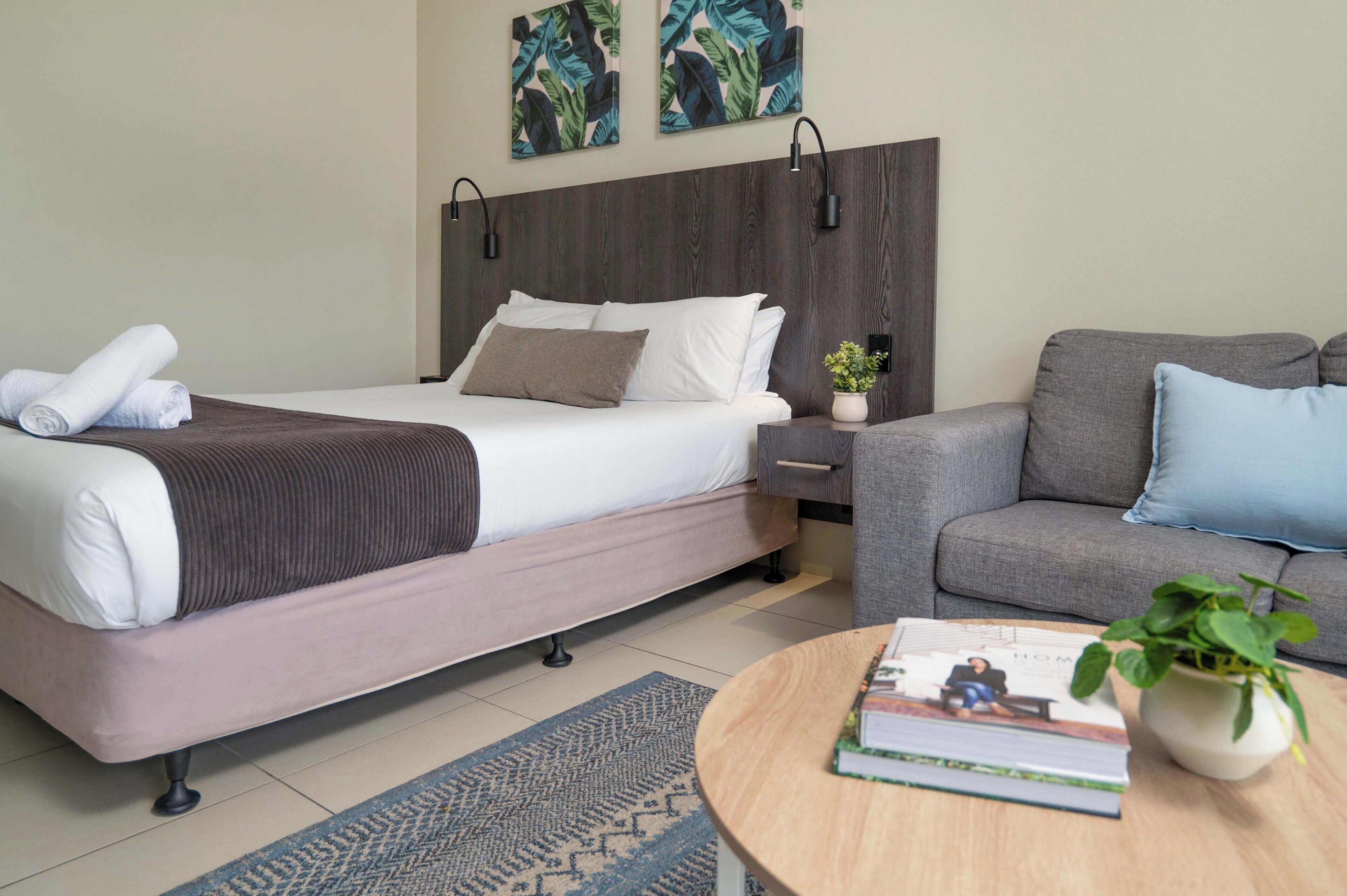 Een hotelkamer met een bed, een bank, een tafeltje met een boek en een plant, en twee wandlampen.