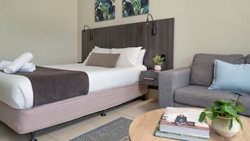 A hotel room with a bed, a sofa, a small table with a book and a plant, and two wall-mounted lamps.