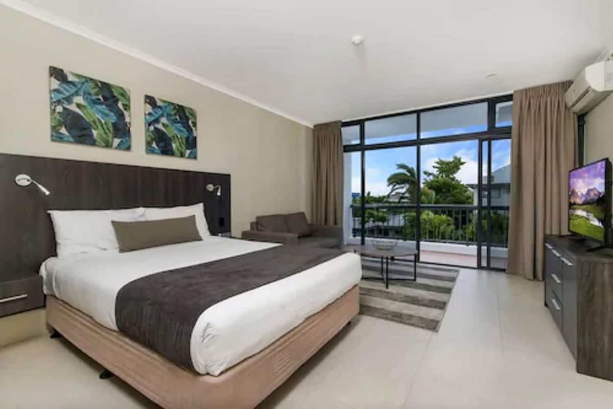 Una habitación de hotel moderna con una cama grande, un televisor de pantalla plana y un balcón con vistas a palmeras.
