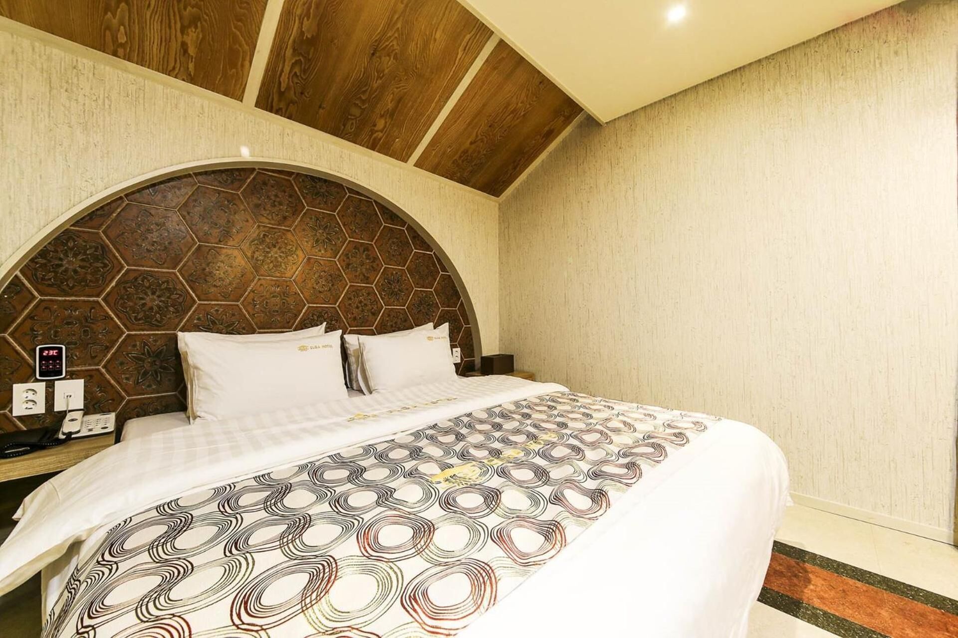 Ein Hotelzimmer mit einem großen Bett, einer Holzbalkendecke und einem sechseckig gemusterten Kopfteil.