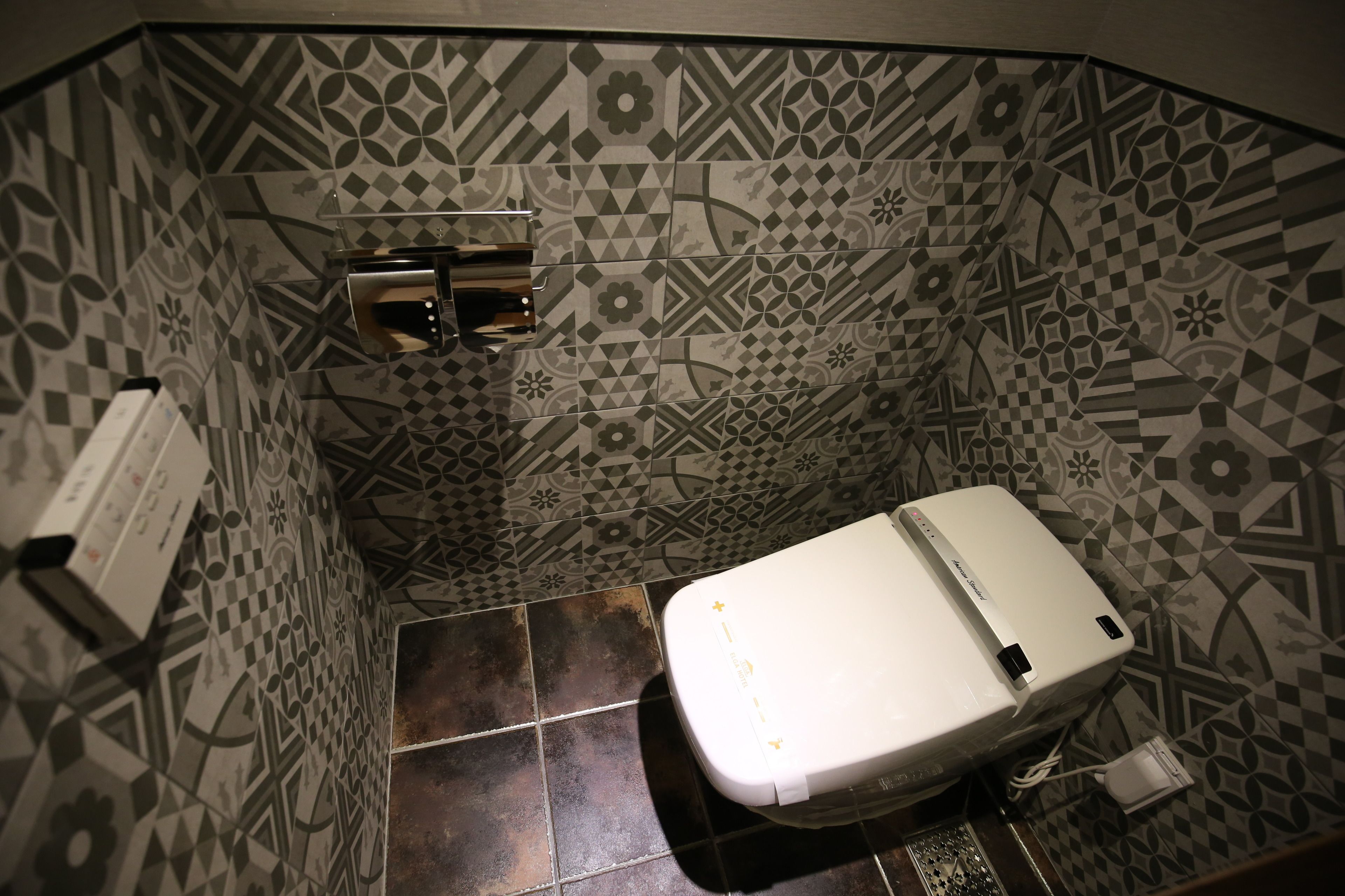 Ein Badezimmer mit gemusterten Fliesen, einer weißen Toilette und einem Handtrockner.