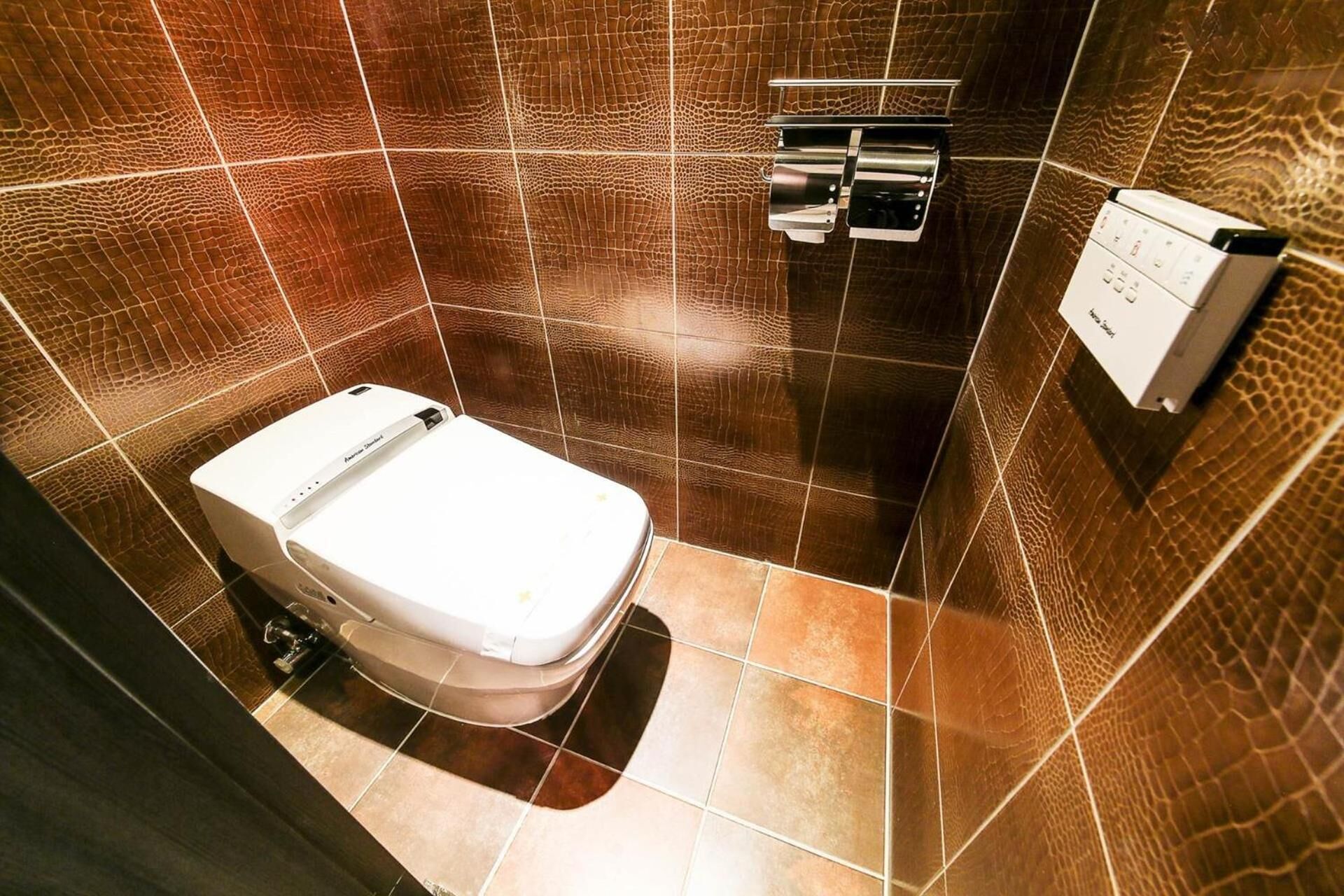 A modern bathroom with a white toilet, a towel rack, and a wall-mounted paper towel dispenser.