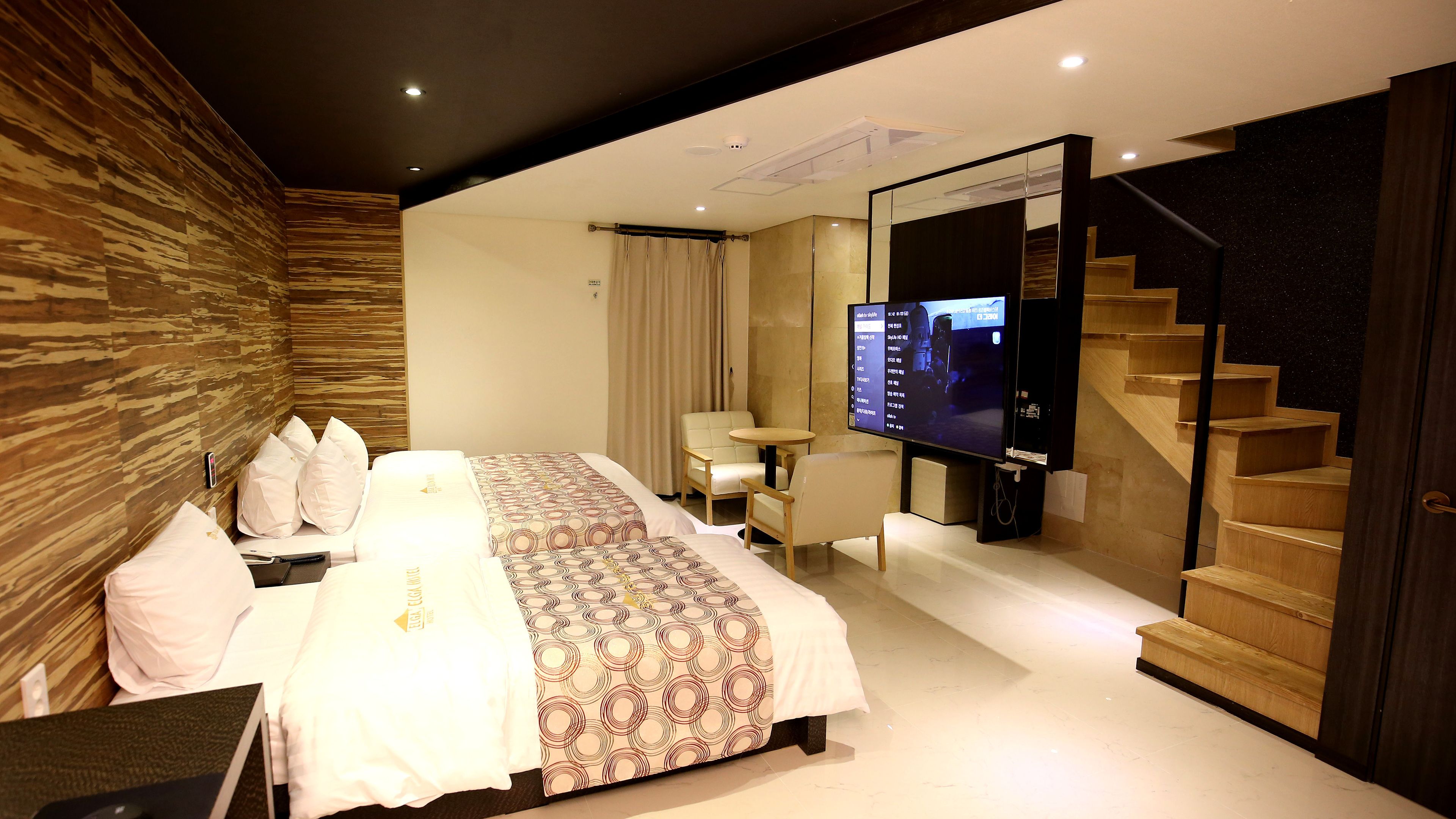 Habitación de hotel moderna con una cama grande, un escritorio, una silla, un televisor y una escalera.
