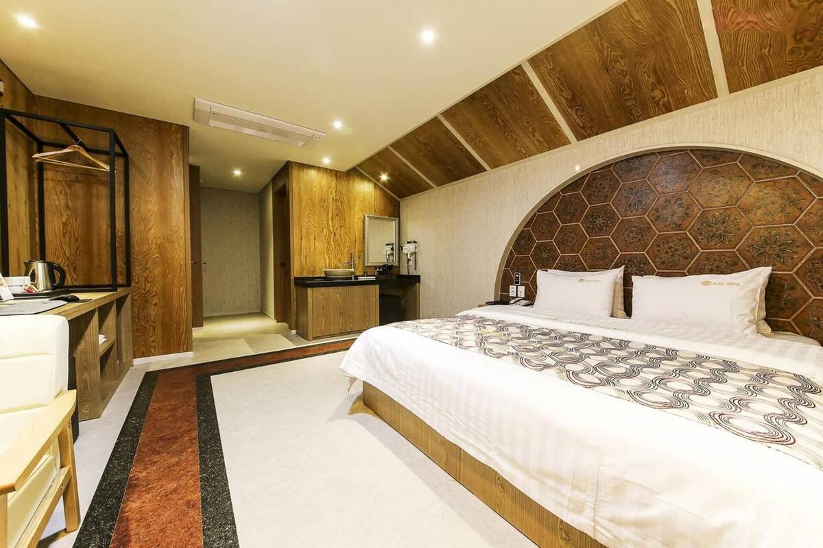 Hotellihuone, jossa on suuri sänky, puinen pääty, työpöytä tuolilla ja taustalla näkyvä kylpyhuone.