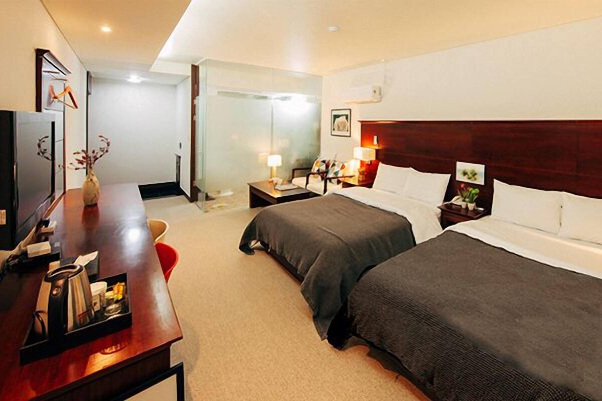 A hotel room with two single beds, a desk with a coffee maker, a TV, and a bedside table with lamps.