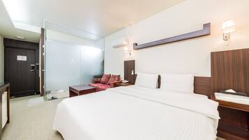 A modern hotel room with a large bed, a desk, a chair, a mirror, and a wardrobe.