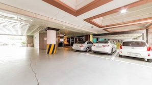 A parking garage with three cars parked in designated spaces, a visible crack on the floor, and a modern ceiling design.