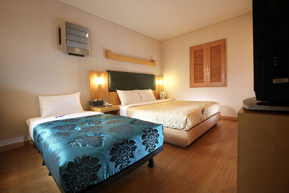 A hotel room with two beds, a desk, a chair, a TV, and a wall-mounted heater.