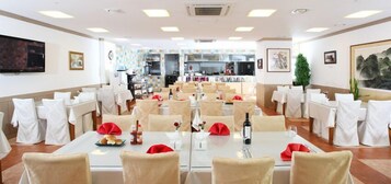 A spacious dining area with multiple tables, chairs, and a kitchen in the background.