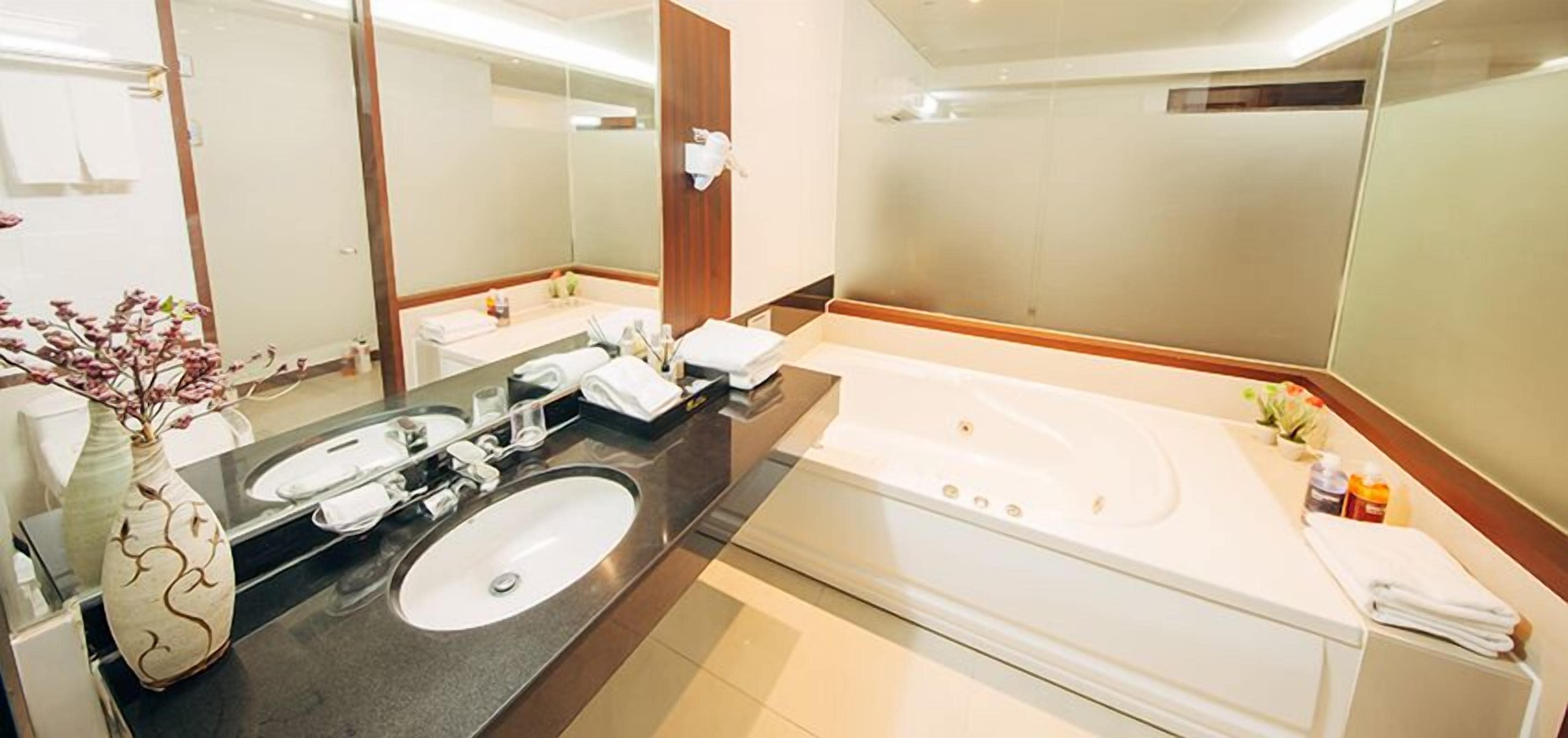 A hotel bathroom with a double sink, a large bathtub, and a mirror.