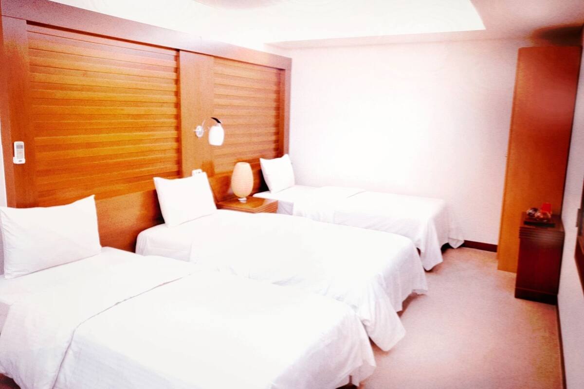A hotel room with two beds, a wooden headboard, a bedside lamp, and a small table.