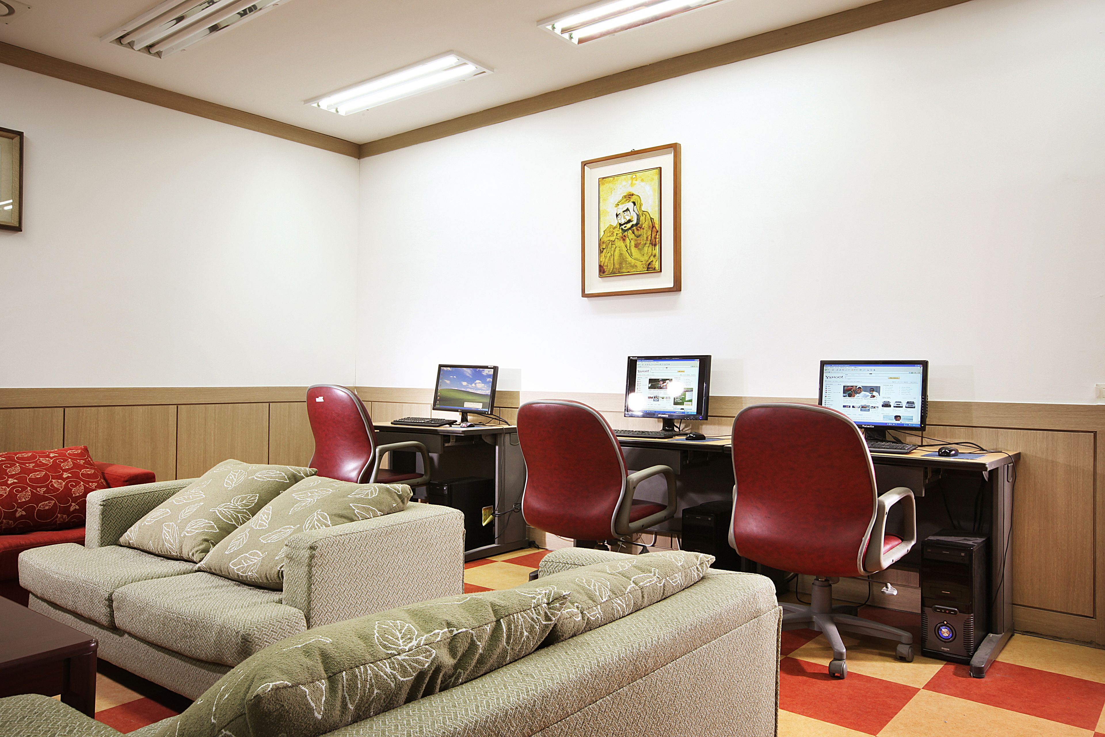 A room with two desks, two chairs, and a sofa with patterned cushions.