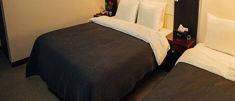 A hotel room with two beds, a nightstand, a small table with a lamp, and a wall-mounted artwork.