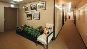 A hallway with a seating area, framed pictures on the wall, and a plant.
