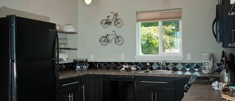 A modern kitchen with black cabinetry, a built-in dishwasher, a granite countertop, and pendant lighting.