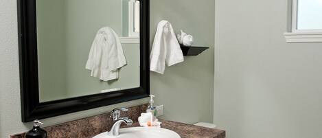 A bathroom with a white sink, a black soap dispenser, a mirror, and a towel rack.