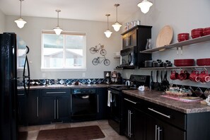 A modern kitchen with black cabinets, a dishwasher, a microwave, and a coffee maker. There are hanging lights, a window, and a bicycle mounted on the wall. - Keystone Vacation Rentals-Ocean View Condos (Depoe Bay)