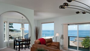 A spacious living room with a large window overlooking the ocean, a dining area with a table and chairs, and a cozy seating area with a leather sofa. - Keystone Vacation Rentals-Ocean View Condos (Depoe Bay)