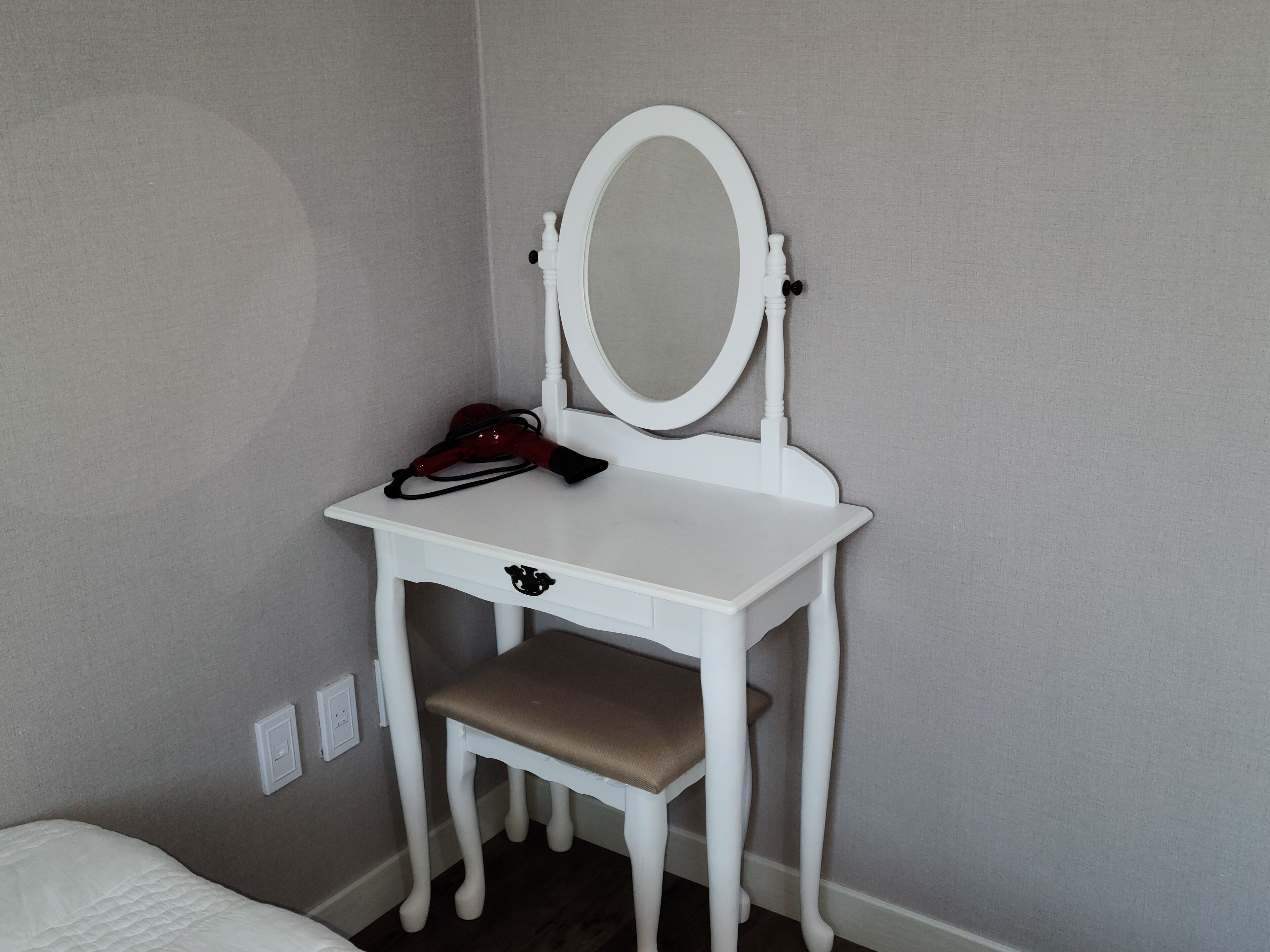 A white vanity with a mirror, a red hairdryer, and a drawer.