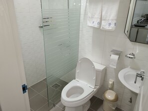 A modern bathroom with a glass shower enclosure, a white toilet, a sink, and a mirror. - Santa Fe Pension (Namhae)