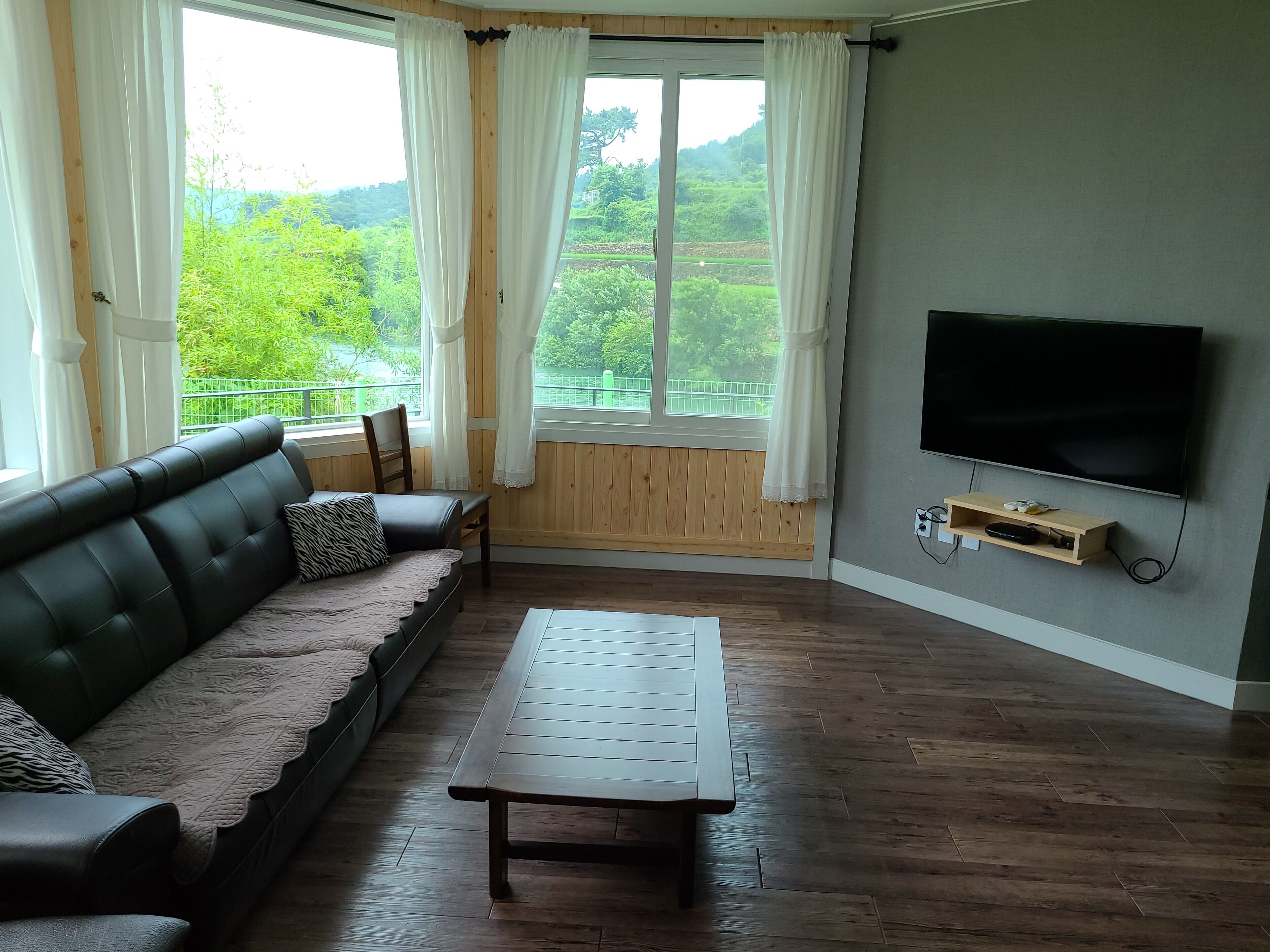 A living room with a black leather sofa, a wooden coffee table, and a TV mounted on the wall.